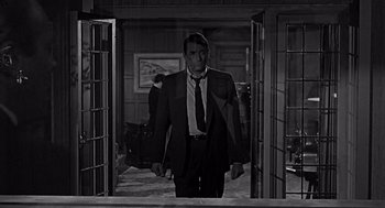 Movie still from “Mirage” (1965), directed by Edward Dmytryk – A black and white photo of a man in a suit and tie; Medium shot, Over the shoulder angle