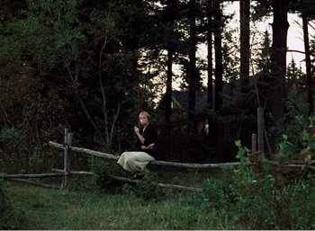 Movie still from “Mirror” (1975), directed by Andrei Tarkovsky – A man sitting on a wooden rail in a yard; Wide shot, High angle