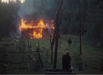 Movie still from “Mirror” (1975), directed by Andrei Tarkovsky – Two people sitting on a bench in front of a burning house; Extreme Wide shot, High angle
