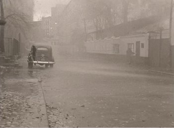Movie still from “Mirror” (1975), directed by Andrei Tarkovsky – An old car is driving down the street in the rain; Wide shot, High angle