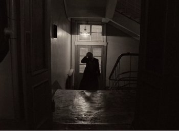 Movie still from “Mirror” (1975), directed by Andrei Tarkovsky – A man standing in a doorway in a dark room; Wide shot, High angle