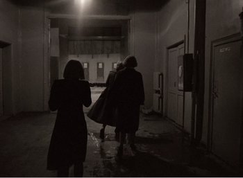 Movie still from “Mirror” (1975), directed by Andrei Tarkovsky – A group of people walking down a hallway at night; Wide shot, Over the shoulder angle