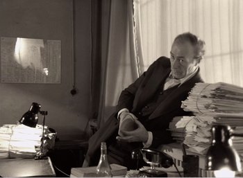 Movie still from “Mirror” (1975), directed by Andrei Tarkovsky – An older man sitting at a table with a stack of papers; Medium shot, High angle