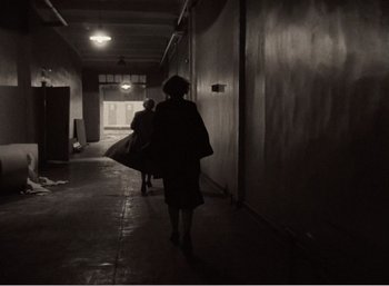 Movie still from “Mirror” (1975), directed by Andrei Tarkovsky – A woman walking down a hallway holding a bag; Wide shot, Over the shoulder angle