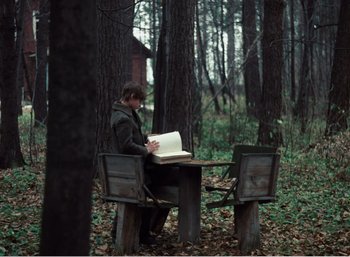 Movie still from “Mirror” (1975), directed by Andrei Tarkovsky – A man sitting at a table in the woods reading; Wide shot, High angle