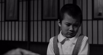 Movie still from “Mishima: A Life in Four Chapters” (1985), directed by Paul Schrader – A young boy in a white shirt and suspenders looks sad; Close Up shot, High angle