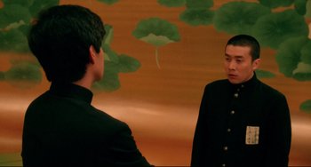 Movie still from “Mishima: A Life in Four Chapters” (1985), directed by Paul Schrader – Two men in black suits are looking at each other in front of a painting; Medium shot, Over the shoulder angle