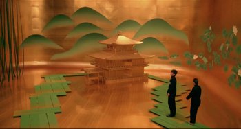 Movie still from “Mishima: A Life in Four Chapters” (1985), directed by Paul Schrader – A man standing in front of a building in the middle of a room; Extreme Wide shot, High angle