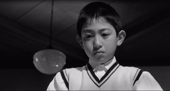 Movie still from “Mishima: A Life in Four Chapters” (1985), directed by Paul Schrader – A young boy in a white shirt is looking at the camera; Close Up shot, Low angle