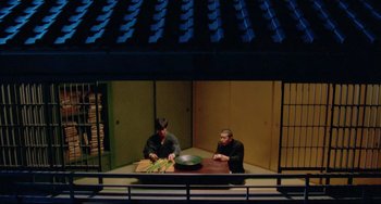Movie still from “Mishima: A Life in Four Chapters” (1985), directed by Paul Schrader – Two men sitting at a table in front of a bowl; Wide shot, High angle