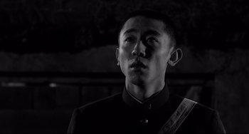 Movie still from “Mishima: A Life in Four Chapters” (1985), directed by Paul Schrader – A man in a black suit looking to his left; Close Up shot, Low angle