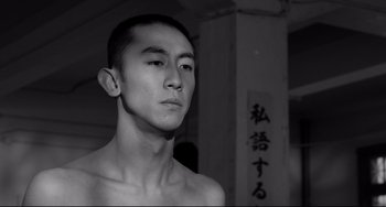 Movie still from “Mishima: A Life in Four Chapters” (1985), directed by Paul Schrader – A young man with a shaved head is posing for a picture; Close Up shot, Low angle