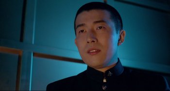 Movie still from “Mishima: A Life in Four Chapters” (1985), directed by Paul Schrader – A man in a black shirt is looking at the camera; Close Up shot, Low angle