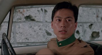 Movie still from “Mishima: A Life in Four Chapters” (1985), directed by Paul Schrader – A man with a green collar sitting in the back of a car; Close Up shot, Low angle