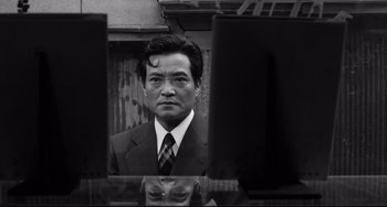 Movie still from “Mishima: A Life in Four Chapters” (1985), directed by Paul Schrader – A black and white photo of a man in a suit looking at himself in the mirror; Close Up shot, Low angle