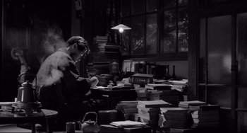 Movie still from “Mishima: A Life in Four Chapters” (1985), directed by Paul Schrader – A man sitting in front of stacks of papers; Medium shot, High angle