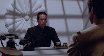 Movie still from “Mishima: A Life in Four Chapters” (1985), directed by Paul Schrader – A man sitting at a table in front of a window; Medium shot, Low angle