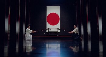 Movie still from “Mishima: A Life in Four Chapters” (1985), directed by Paul Schrader – Two people are practicing martial arts in front of a japanese flag; Extreme Wide shot, High angle