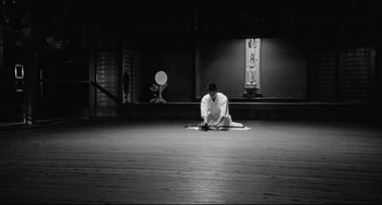 Movie still from “Mishima: A Life in Four Chapters” (1985), directed by Paul Schrader – A man kneeling on the ground in a room; Wide shot, High angle