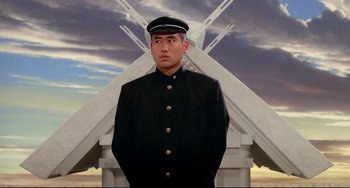 Movie still from “Mishima: A Life in Four Chapters” (1985), directed by Paul Schrader – A man in a uniform standing in front of a building; Medium shot, Low angle