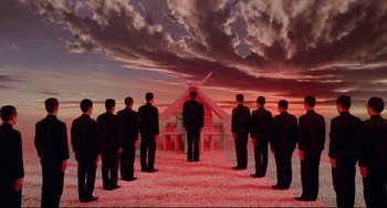 Movie still from “Mishima: A Life in Four Chapters” (1985), directed by Paul Schrader – A group of men standing in front of a building under a cloudy sky; Extreme Wide shot, Low angle