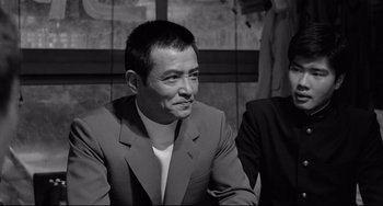 Movie still from “Mishima: A Life in Four Chapters” (1985), directed by Paul Schrader – Black and white photograph of a man wearing a suit; Close Up shot, Over the shoulder angle