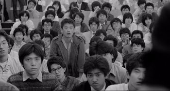 Movie still from “Mishima: A Life in Four Chapters” (1985), directed by Paul Schrader – A large group of young men sitting in a room; Medium shot, High angle