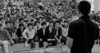 Movie still from “Mishima: A Life in Four Chapters” (1985), directed by Paul Schrader – A group of young men sitting in front of an audience; Medium shot, High angle