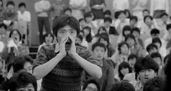 Movie still from “Mishima: A Life in Four Chapters” (1985), directed by Paul Schrader – A woman covering her mouth in front of a group of people; Close Up shot, High angle