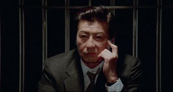 Movie still from “Mishima: A Life in Four Chapters” (1985), directed by Paul Schrader – A man in a suit sitting in front of a cell phone; Close Up shot, High angle