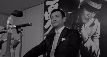 Movie still from “Mishima: A Life in Four Chapters” (1985), directed by Paul Schrader – A black and white photo of a man in a suit and tie; Medium shot, Low angle