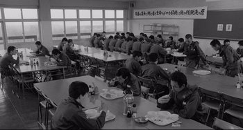 Movie still from “Mishima: A Life in Four Chapters” (1985), directed by Paul Schrader – A black and white photo of people sitting at a table eating food; Wide shot, High angle
