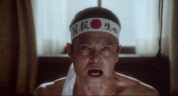 Movie still from “Mishima: A Life in Four Chapters” (1985), directed by Paul Schrader – A person wearing a headband; Close Up shot, Low angle