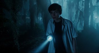 Movie still from “Miss Peregrine's Home for Peculiar Children” (2016), directed by Tim Burton – A young man is holding a flashlight in the woods; Medium shot, High angle