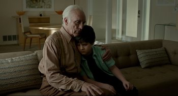 Movie still from “Miss Peregrine's Home for Peculiar Children” (2016), directed by Tim Burton – An older man sitting on the arm of a young boy; Medium shot, High angle