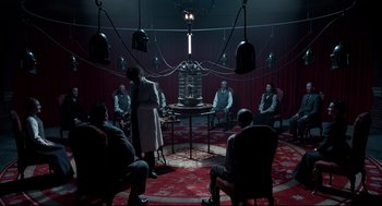 Movie still from “Miss Peregrine's Home for Peculiar Children” (2016), directed by Tim Burton – A group of people sitting in a room with lights; Wide shot, Low angle