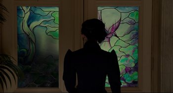 Movie still from “Miss Peregrine's Home for Peculiar Children” (2016), directed by Tim Burton – A woman standing in front of two stained glass windows; Medium shot, Over the shoulder angle