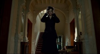 Movie still from “Miss Peregrine's Home for Peculiar Children” (2016), directed by Tim Burton – A woman standing in front of a staircase in a room; Medium shot, Low angle