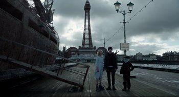 Movie still from “Miss Peregrine's Home for Peculiar Children” (2016), directed by Tim Burton – Three people standing on a pier in front of a tall tower; Wide shot, Low angle