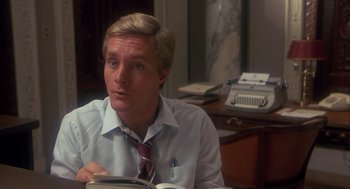 Movie still from “Missing” (1982), directed by Costa-Gavras – A man sitting at a table with a book in front of him; Close Up shot, Over the shoulder angle