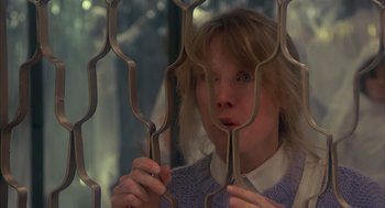 Movie still from “Missing” (1982), directed by Costa-Gavras – A woman looking through a metal fence; Close Up shot, Low angle
