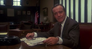 Movie still from “Missing” (1982), directed by Costa-Gavras – A man sitting at a table with papers in front of him; Medium shot, Low angle