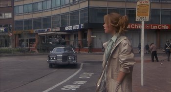 Movie still from “Missing” (1982), directed by Costa-Gavras – A woman is walking down the street in front of a car; Wide shot, Over the shoulder angle
