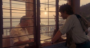 Movie still from “Missing” (1982), directed by Costa-Gavras – A man standing in front of a window looking at another man; Medium shot, Over the shoulder angle