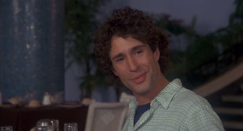 Movie still from “Missing” (1982), directed by Costa-Gavras – A man with curly brown hair smiling for the camera; Close Up shot, Over the shoulder angle