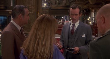 Movie still from “Missing” (1982), directed by Costa-Gavras – A man in a suit and tie talking to two women; Medium shot, Over the shoulder angle