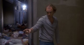 Movie still from “Missing” (1982), directed by Costa-Gavras – A man with a shaved head is holding his hand out; Medium shot, Over the shoulder angle