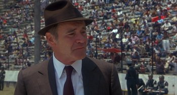 Movie still from “Missing” (1982), directed by Costa-Gavras – A man in a suit and a hat in front of an audience; Close Up shot, Over the shoulder angle