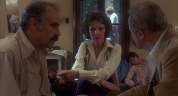 Movie still from “Missing” (1982), directed by Costa-Gavras – A group of people sitting in a living room talking; Medium shot, Over the shoulder angle