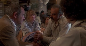 Movie still from “Missing” (1982), directed by Costa-Gavras – A group of people sitting around each other in a room; Medium shot, High angle